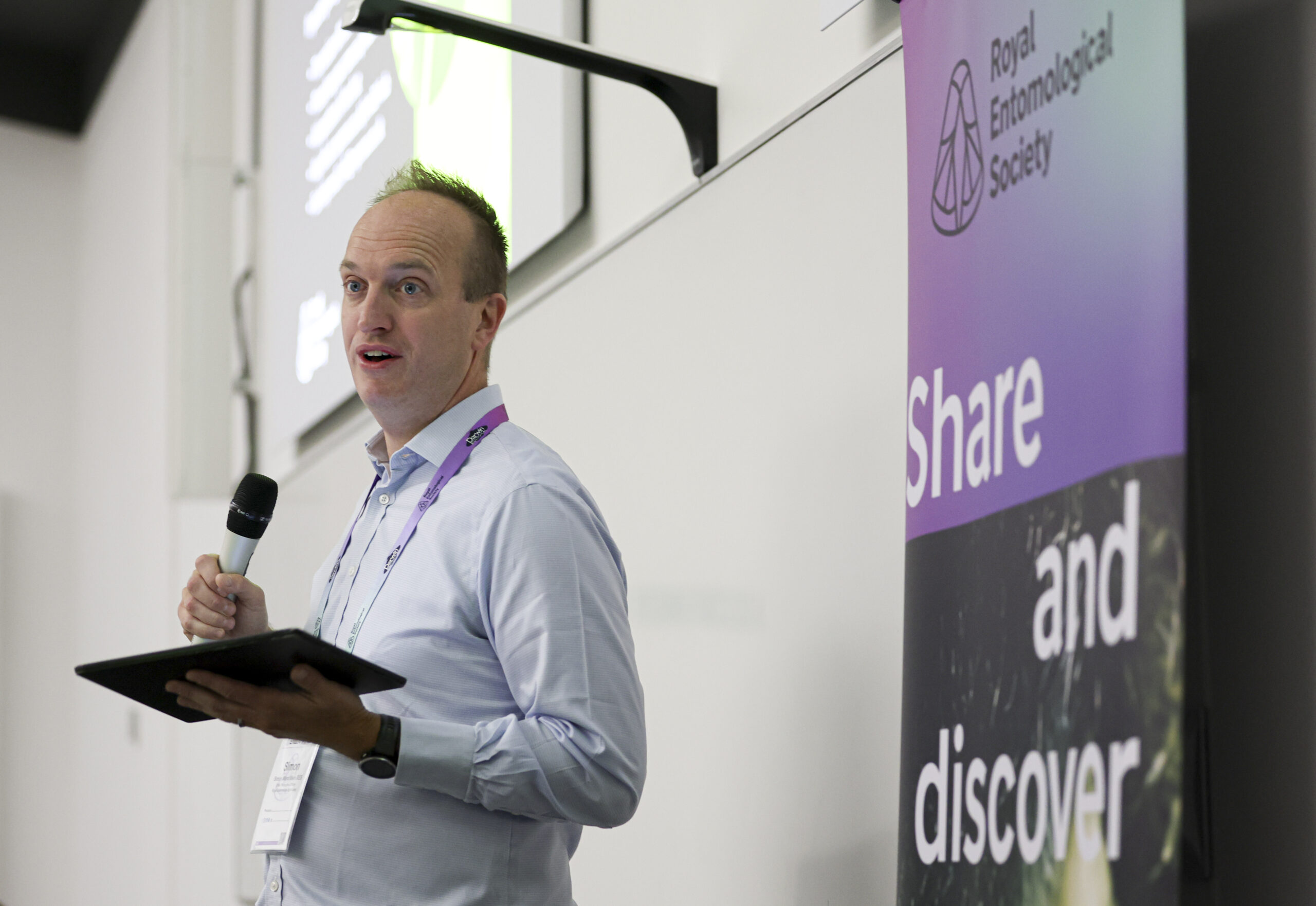 Simon Ward, RES CEO, stood in front of a 'Share and discover' RES branded banner with a microphone introducing the audience to a conference