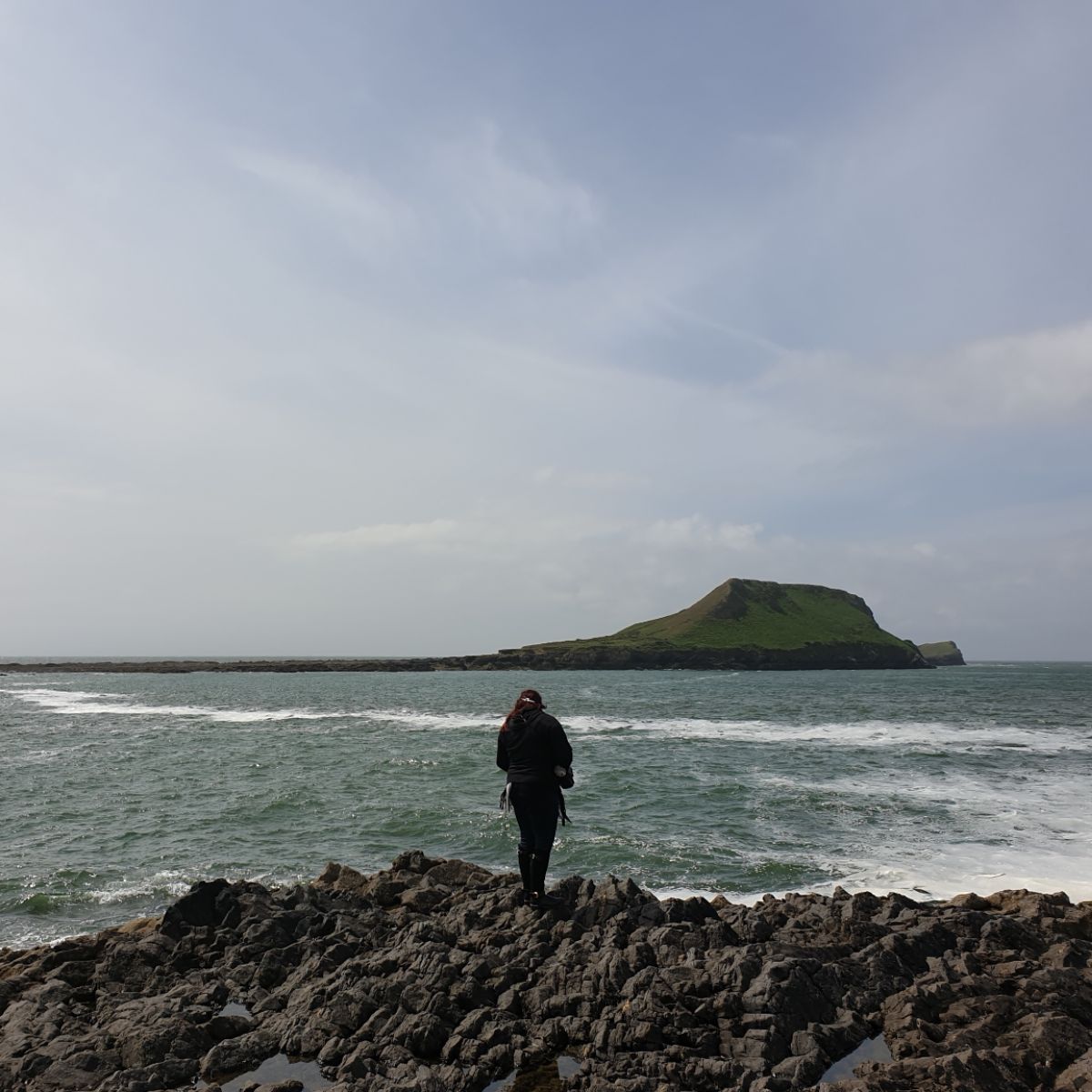 Person standing on the rocks watching the waves at Worms Head, the Gower, Wales