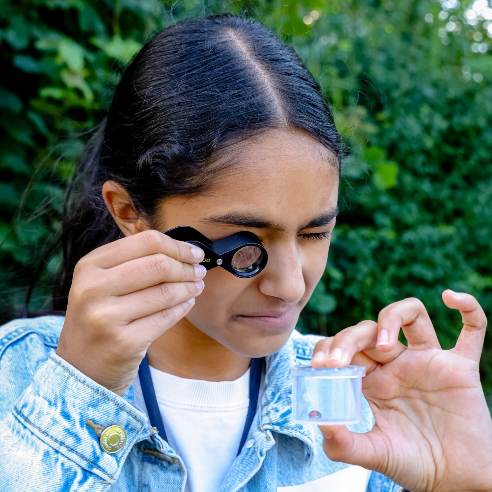 Young person looking into a pot containing an insect