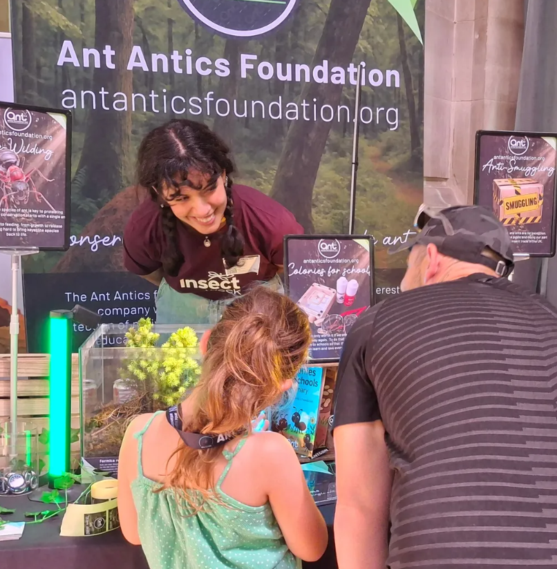 A member of the Insect Week team at Cardff City Hub speaking to two visitors at a stand - Insect Week 2026