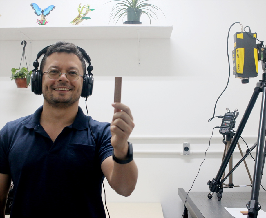Image 1. Lirio Cosme presenting a wood piece, with the laser Doppler vibrometer system configured for the acquisition of vibratory cues. Photo Credit: Leo Turchen